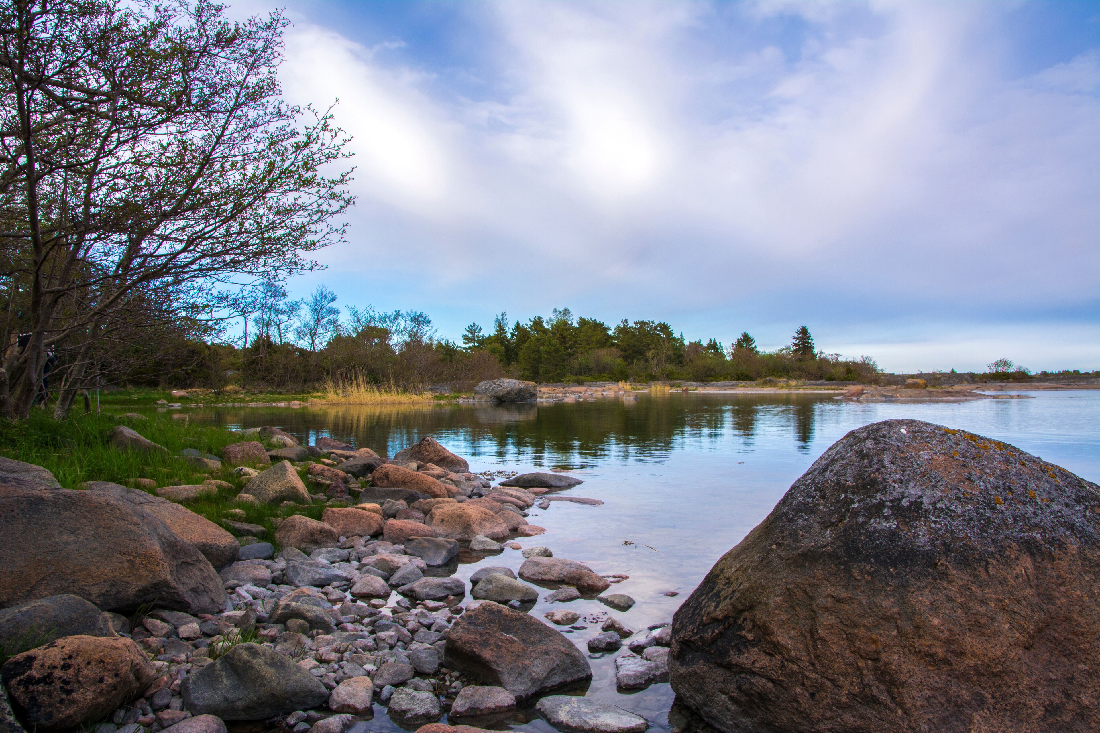 A calm lake with large rocks and trees along the shore.