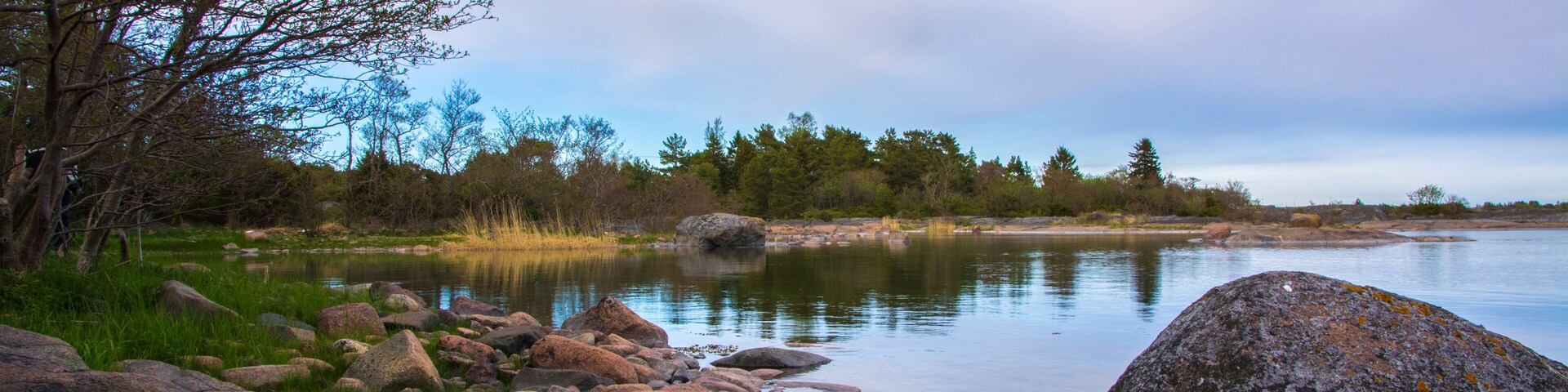A calm lake with large rocks and trees along the shore.
