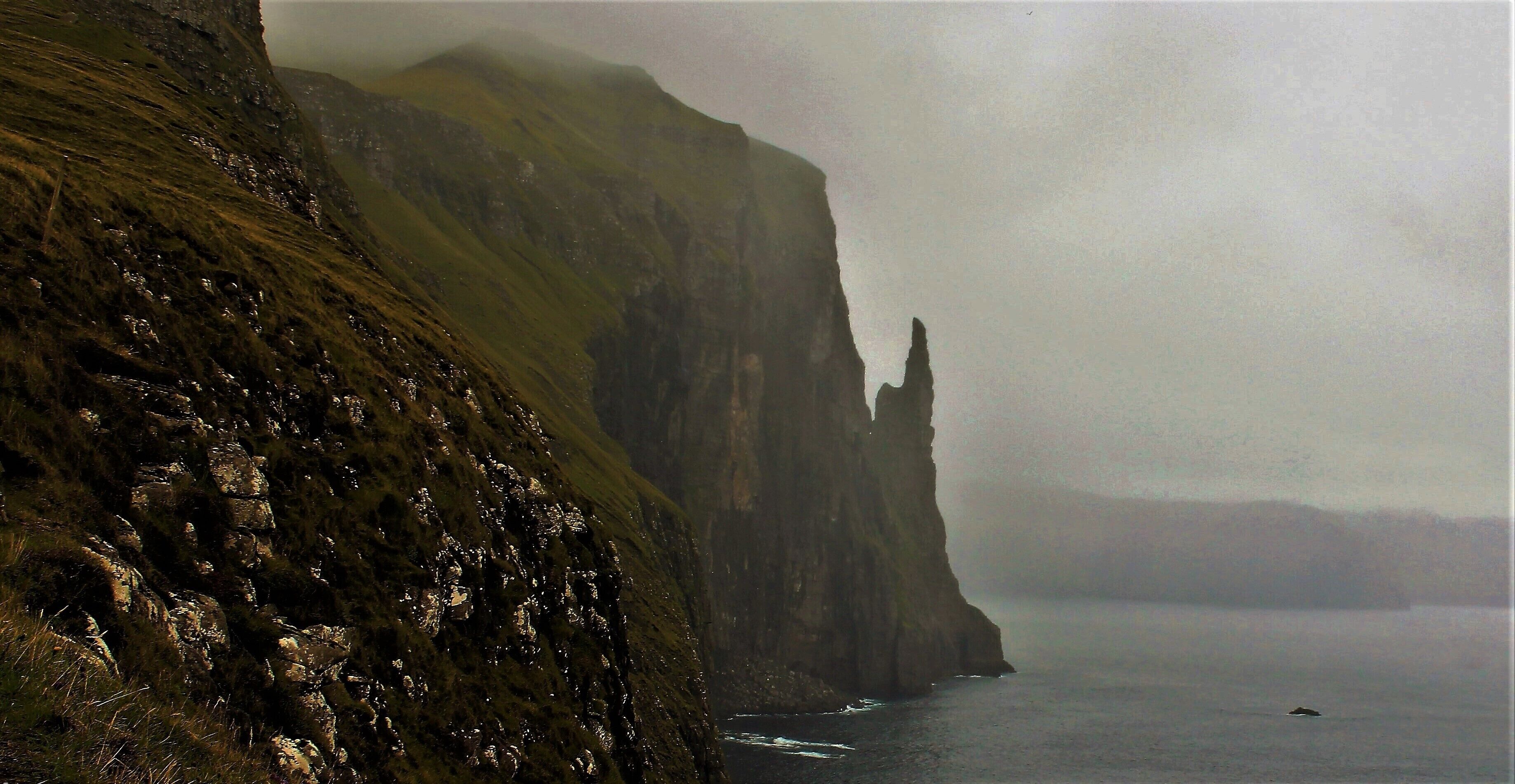 Took this photo 2 weeks ago. One of the best sights on Vágar Island! Trøllkonufingur, which means the Troll woman’s finger, is a 313 m tall monolith on the south-east side of Sandavágur. Only 11 people are known to have reached the top.

Legend has it, that Trøllkonufingur is the finger of a witch that came to throw the Faroe Islands to Iceland. When she came to the sea south of Vágar, the sun came up and she was turned into stone and fell into the ocean.

She was so big that when she reached the bottom of the sea, the back of her head and her finger were above the surface. The back of her head is the island of Koltur, and the finger is Trøllkonufingur.

It is said that in 1844 a member of the Danish royal entourage climbed Trøllkonufingur. At the top he waved to Crown Prince Frederik, as he sailed past it. As climbing down, he realized that he had left one of his gloves at the top. He decided to climb up again to get it. Having just climbed it the first time he was tired and stumbled and fell into his death. Thanks for the great information: http://visitvagar.fo/welcome-to-vagar/about/stories-and-legends/troellkonufingur/