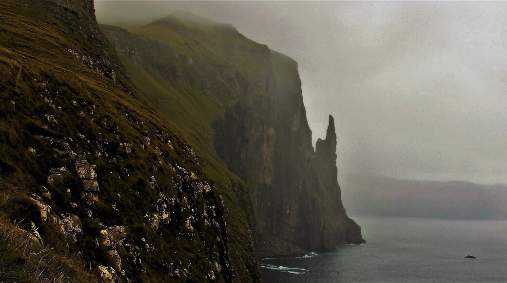 Took this photo 2 weeks ago. One of the best sights on Vágar Island! Trøllkonufingur, which means the Troll woman’s finger, is a 313 m tall monolith on the south-east side of Sandavágur. Only 11 people are known to have reached the top.
Legend has it, that Trøllkonufingur is the finger of a witch that came to throw the Faroe Islands to Iceland. When she came to the sea south of Vágar, the sun came up and she was turned into stone and fell into the ocean.
She was so big that when she reached the bottom of the sea, the back of her head and her finger were above the surface. The back of her head is the island of Koltur, and the finger is Trøllkonufingur.
It is said that in 1844 a member of the Danish royal entourage climbed Trøllkonufingur. At the top he waved to Crown Prince Frederik, as he sailed past it. As climbing down, he realized that he had left one of his gloves at the top. He decided to climb up again to get it. Having just climbed it the first time he was tired and stumbled and fell into his death. Thanks for the great information: http://visitvagar.fo/welcome-to-vagar/about/stories-and-legends/troellkonufingur/