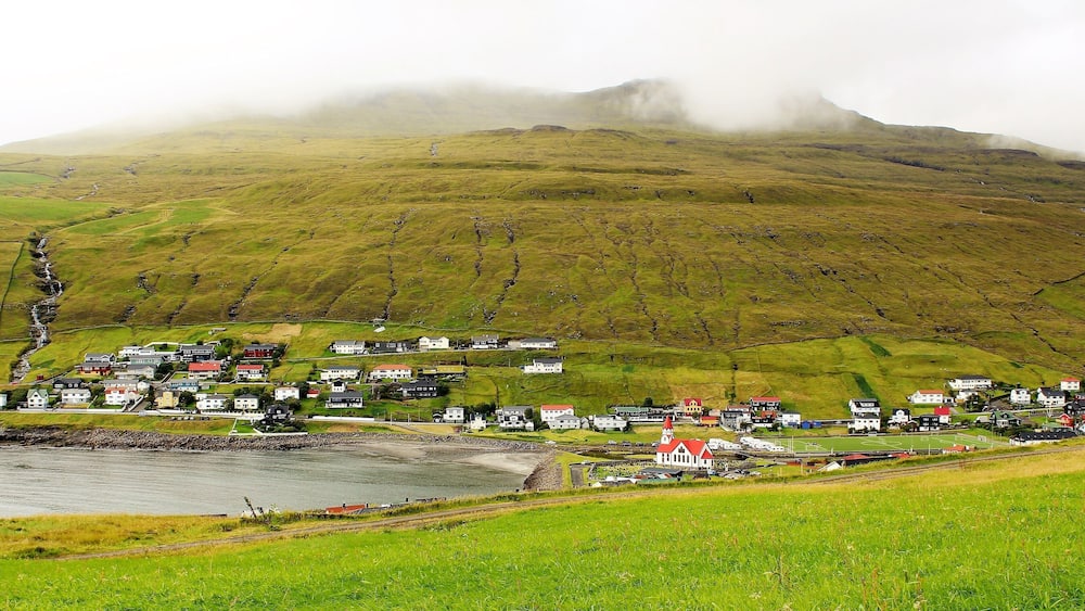 An idyllic, misty view of Sandavágur! I was on my way to the otherworldly Trøllkonufingur! Trøllkonufingur was one of the best sights on Vágar Island and one of the highlights of my trip. But, I also enjoyed the walk to and from there! I hiked about 12 KM that entire day and it was well worth it.
Sandavágur has been voted the most well-kept village in the Faroes twice. And it's the most famous "city" in the country, and best voted traveling experience. Although, not an actual city at all - the population is only around 861! The name Sandavágur means sandy bay and refers to the sandy beach which used to be much larger than present. From one point in Sandavágur you can get a view of all the southern islands in the Faroes. And the red-roofed church seen in this photo is one of the best in the Faroe Islands! In fact, members of the Danish Royal Family were there 1 day after I was! I even saw their motorcade as they were continuing on their journey. A pretty cool experience, too ;).
I took this photo on August 25th.