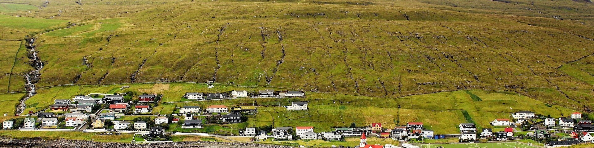 An idyllic, misty view of Sandavágur! I was on my way to the otherworldly Trøllkonufingur! Trøllkonufingur was one of the best sights on Vágar Island and one of the highlights of my trip. But, I also enjoyed the walk to and from there! I hiked about 12 KM that entire day and it was well worth it.
Sandavágur has been voted the most well-kept village in the Faroes twice. And it's the most famous "city" in the country, and best voted traveling experience. Although, not an actual city at all - the population is only around 861! The name Sandavágur means sandy bay and refers to the sandy beach which used to be much larger than present. From one point in Sandavágur you can get a view of all the southern islands in the Faroes. And the red-roofed church seen in this photo is one of the best in the Faroe Islands! In fact, members of the Danish Royal Family were there 1 day after I was! I even saw their motorcade as they were continuing on their journey. A pretty cool experience, too ;).
I took this photo on August 25th.
