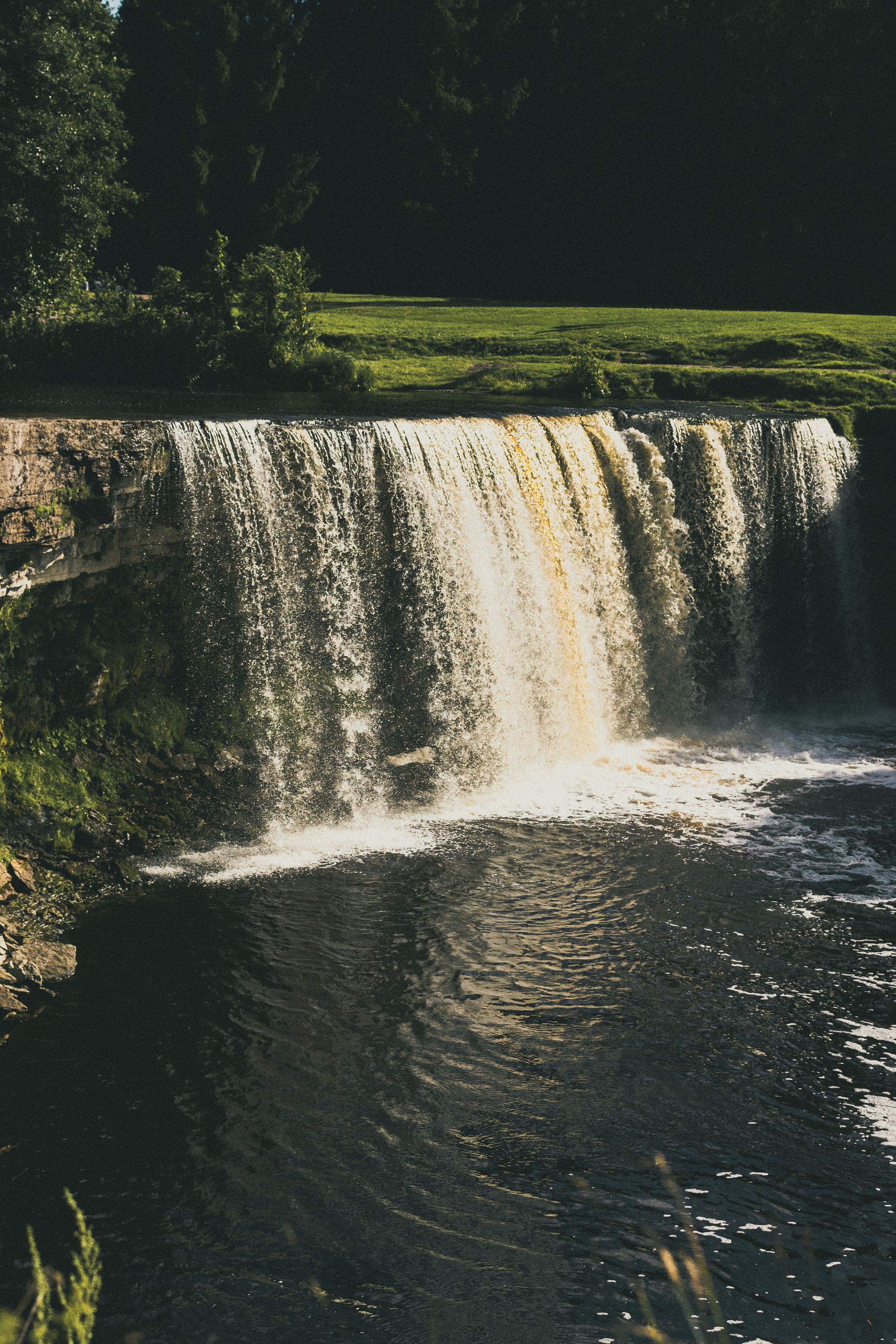 Ein Wasserfall stürzt über einen Felsen in einen ruhigen Fluss.