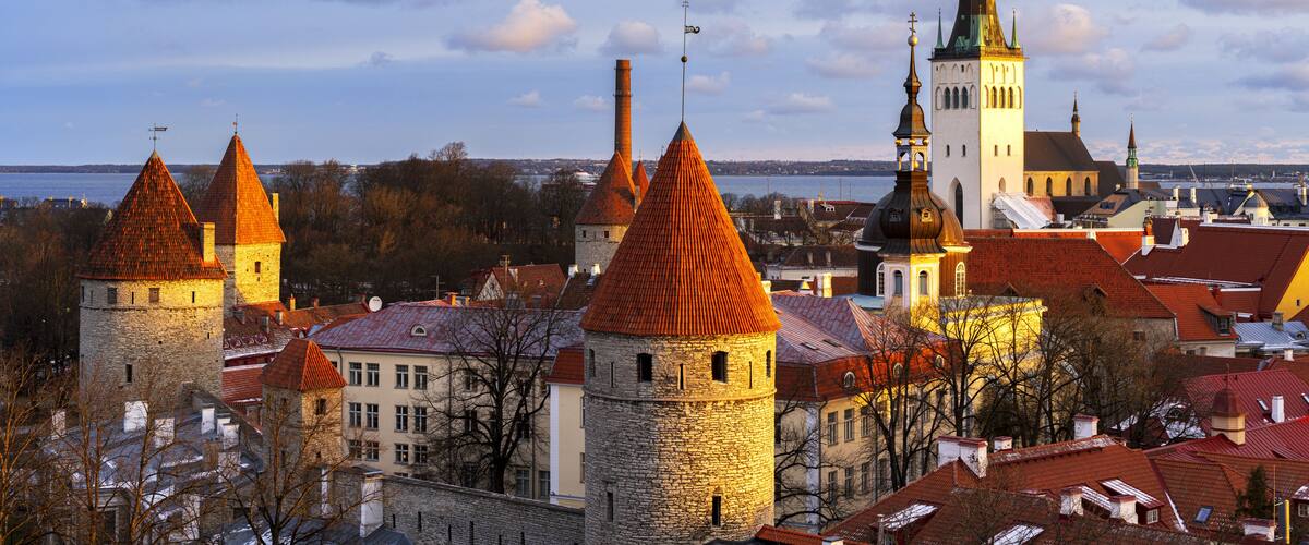 View of the historic Tallinn Old Town with medieval towers, red-tiled rooftops, and the spire of St. Olaf's Church illuminated by golden hour light in Tallinn, Harju County, Estonia.