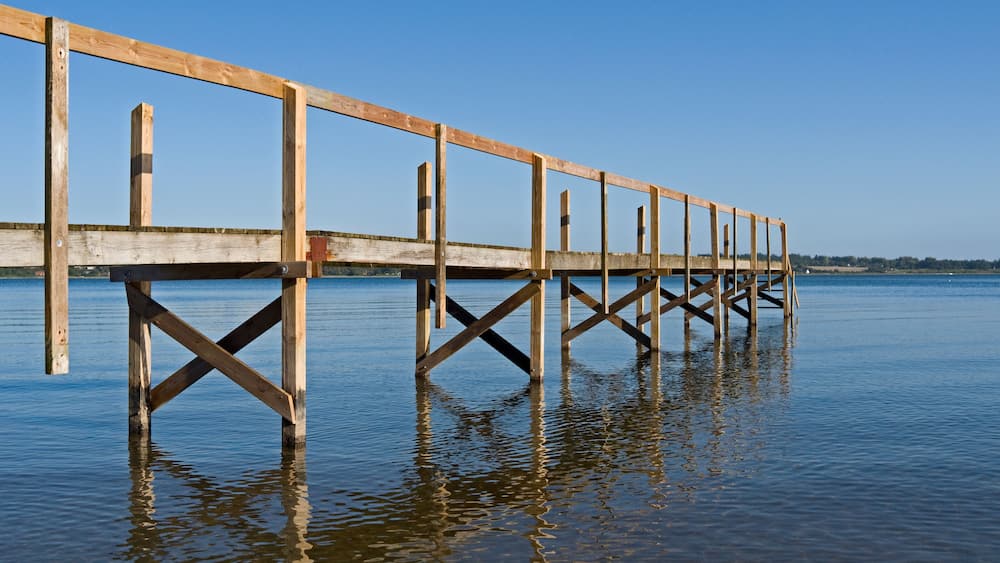 A wooden pier extending into calm water with a clear sky.
