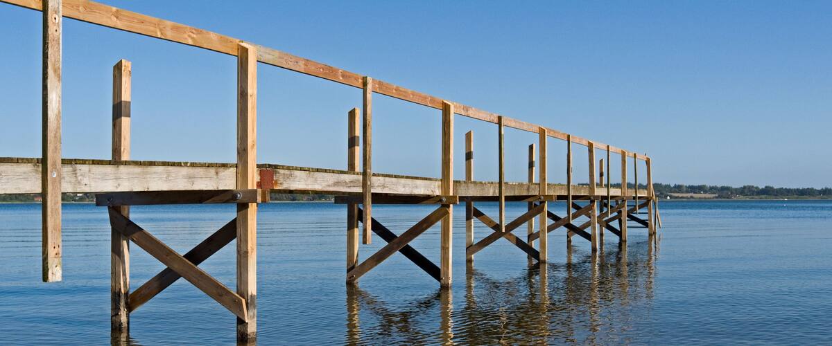A wooden pier extending into calm water with a clear sky.