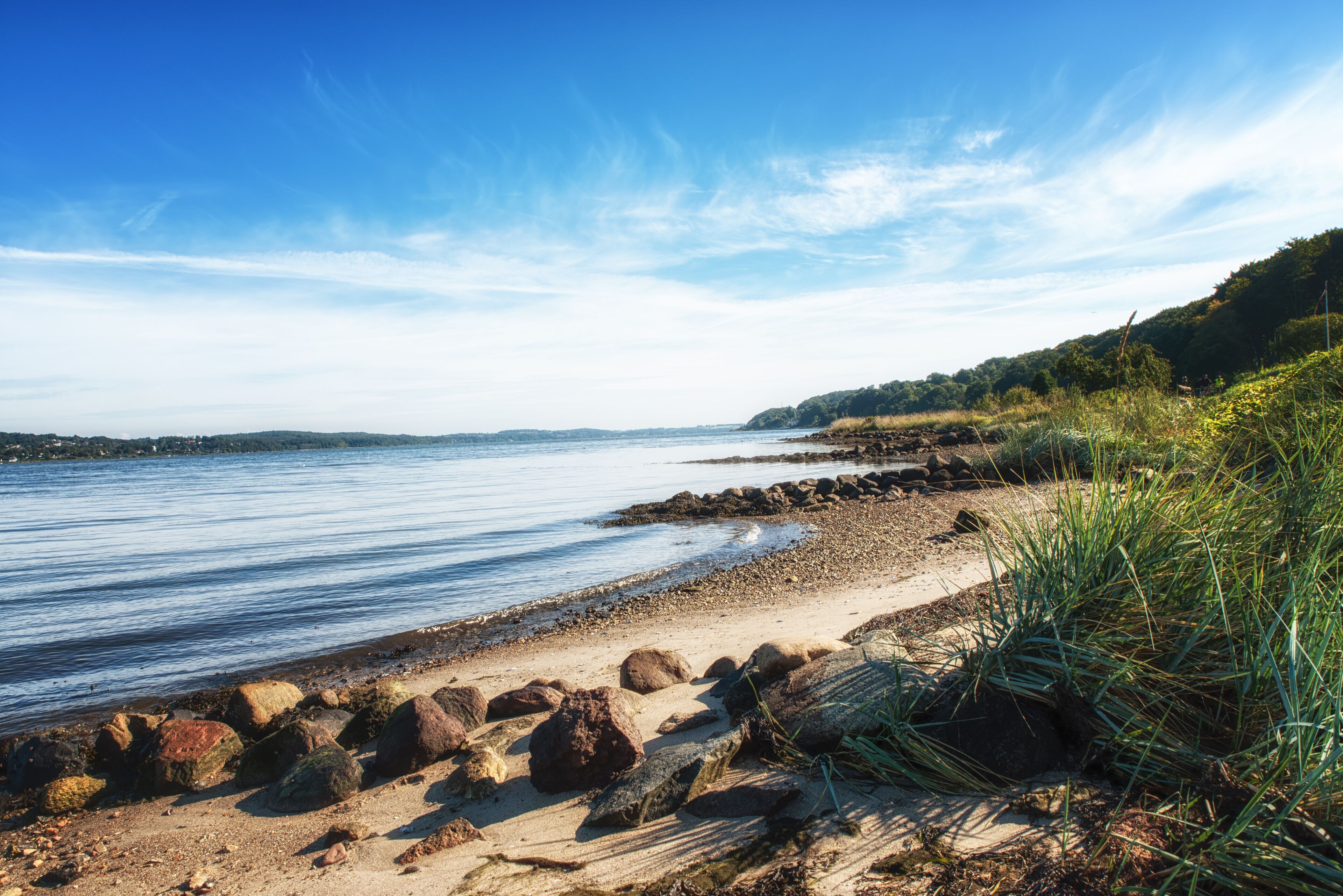 A coastal landscape with a sandy beach, large rocks, and a calm body of water.