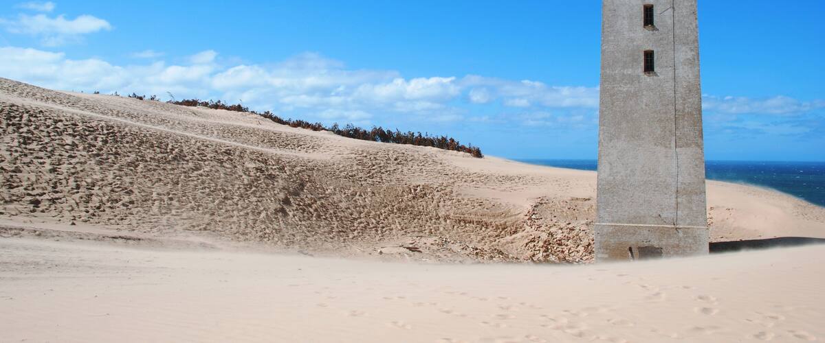 A lighthouse on a sandy beach with a clear blue sky.
