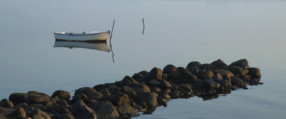 A calm lake with a small boat anchored near a rocky shore.