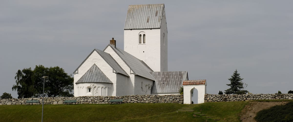 A white church with a bell tower and a stone wall.