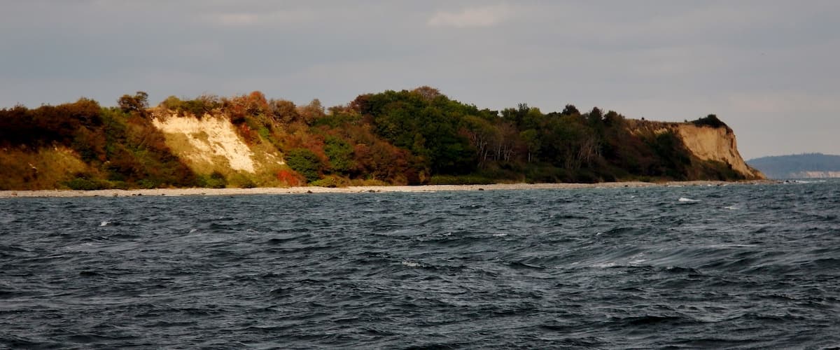 A coastal landscape with a sandy beach, rocky cliffs, and dense vegetation.