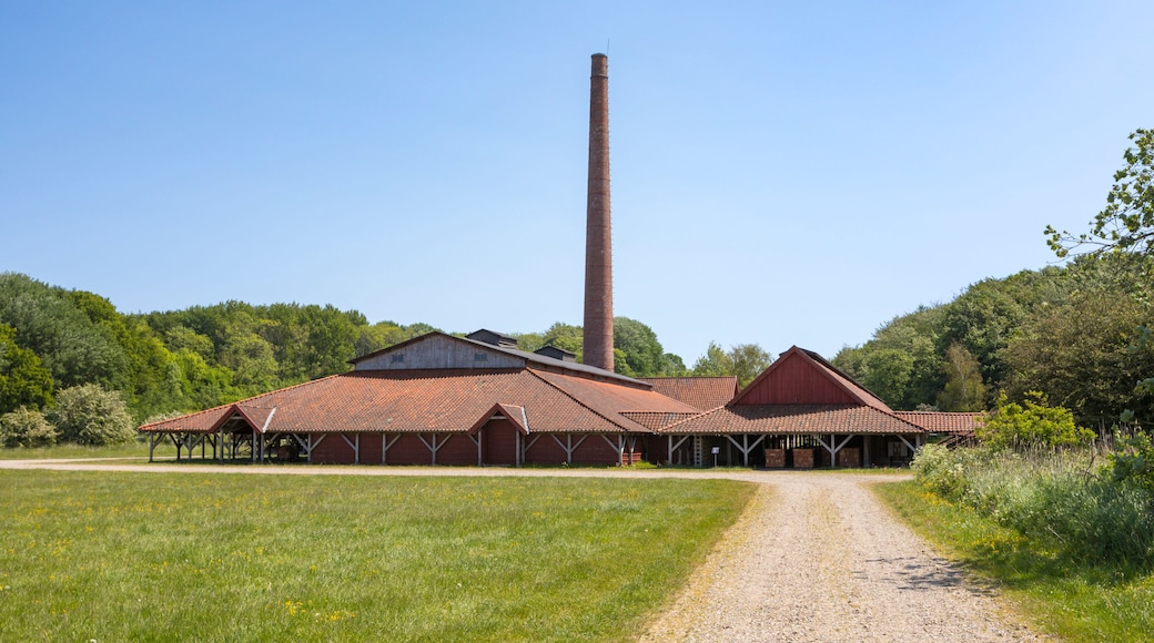 A rural landscape with a large red barn, a tall chimney, and a gravel path leading to the barn.