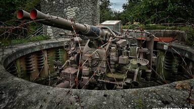 A large artillery piece in a concrete bunker with barbed wire.