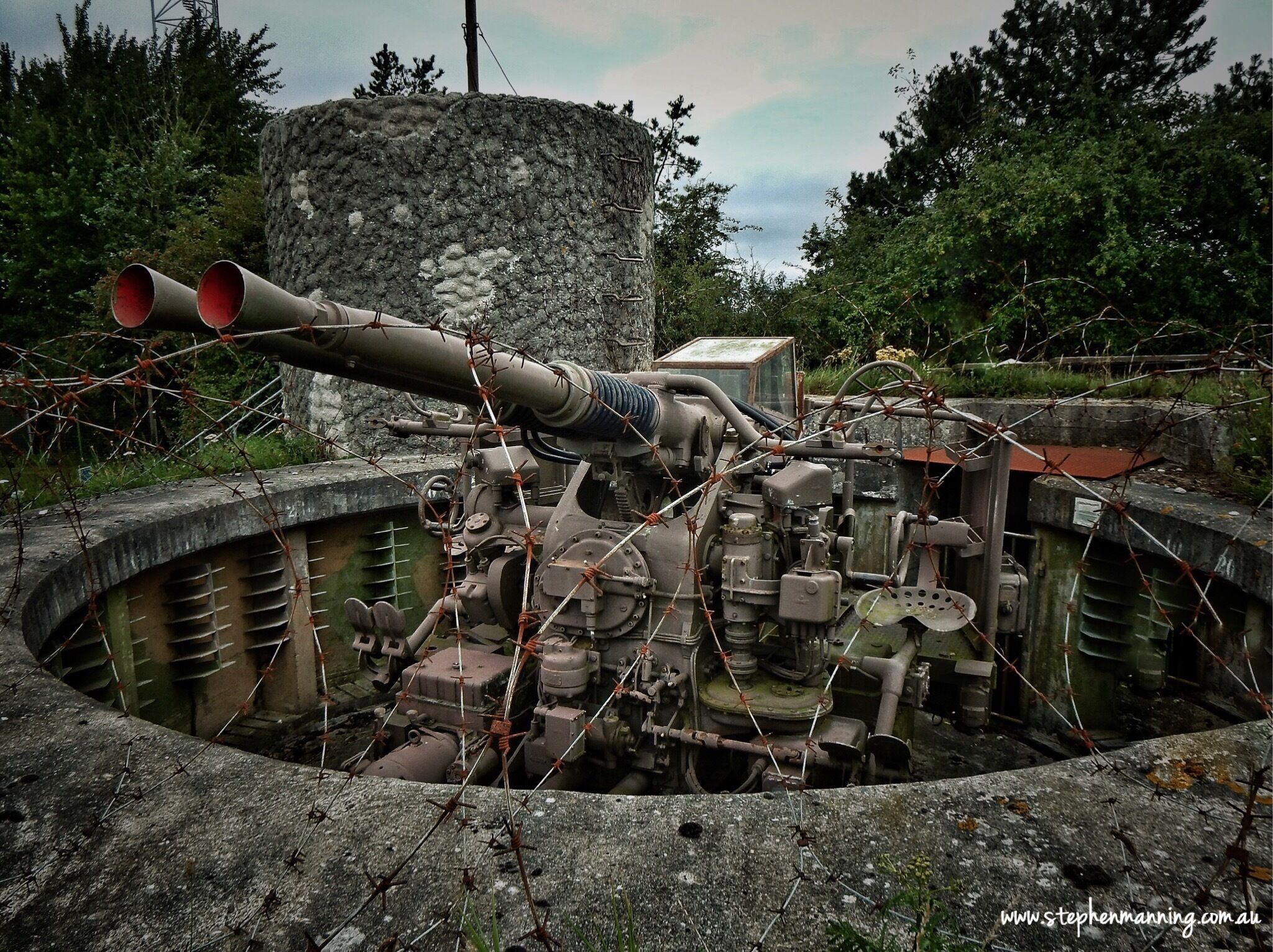 A large artillery piece in a concrete bunker with barbed wire.