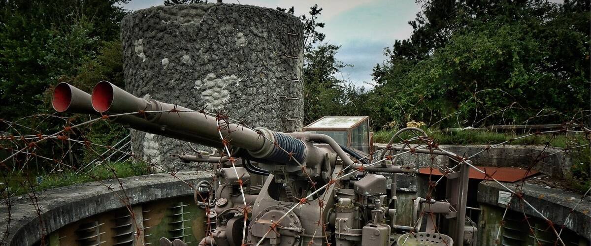 A large artillery piece in a concrete bunker with barbed wire.