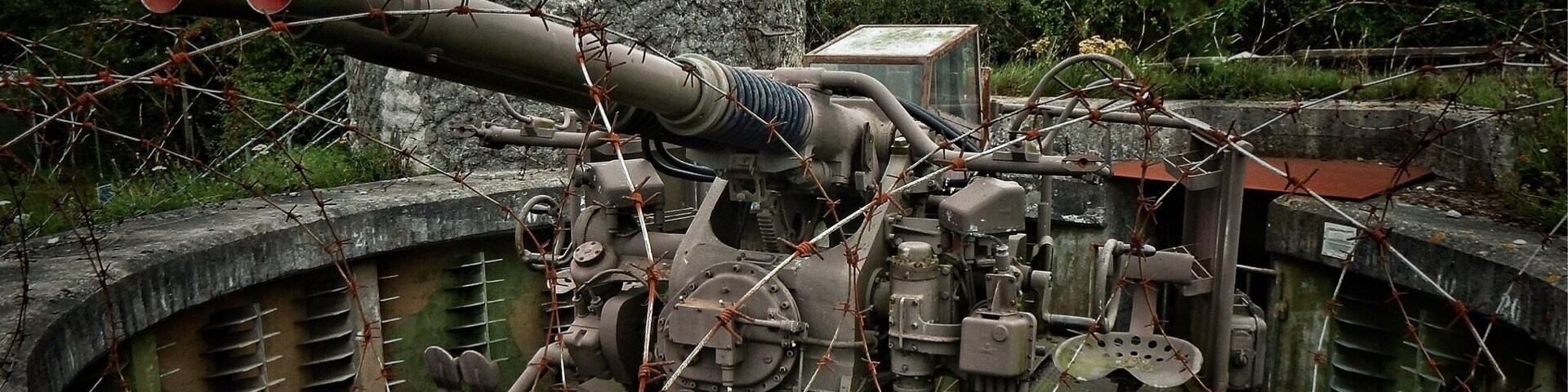 A large artillery piece in a concrete bunker with barbed wire.