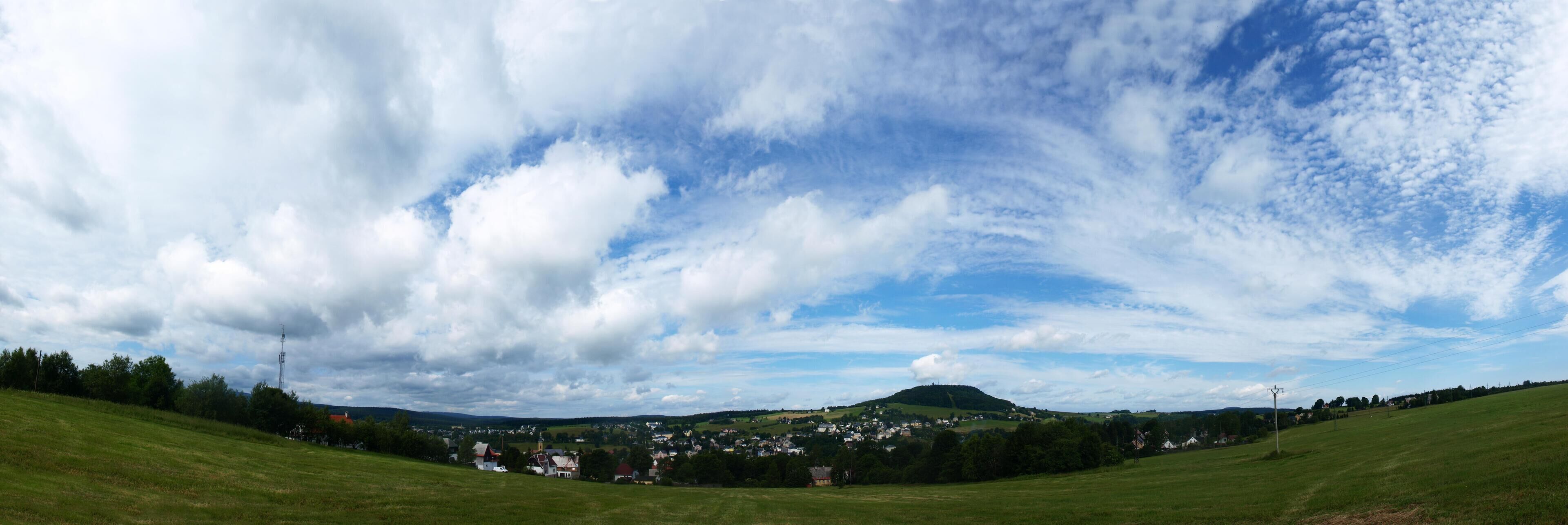 A panoramic view of a town nestled in a valley with rolling hills and a prominent hill in the background.