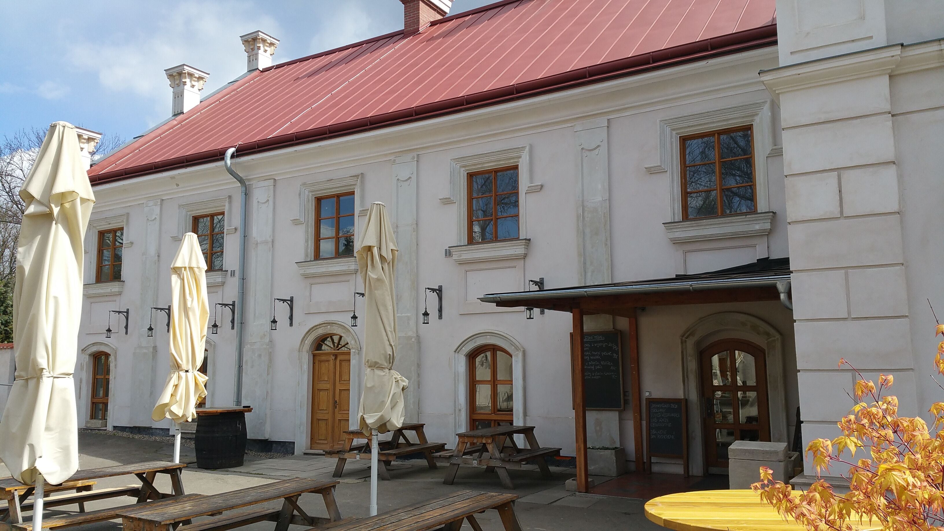 A white building with a red roof, outdoor tables, and umbrellas.