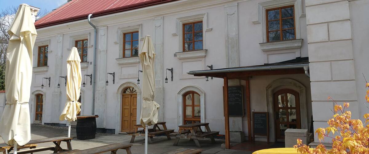 A white building with a red roof, outdoor tables, and umbrellas.