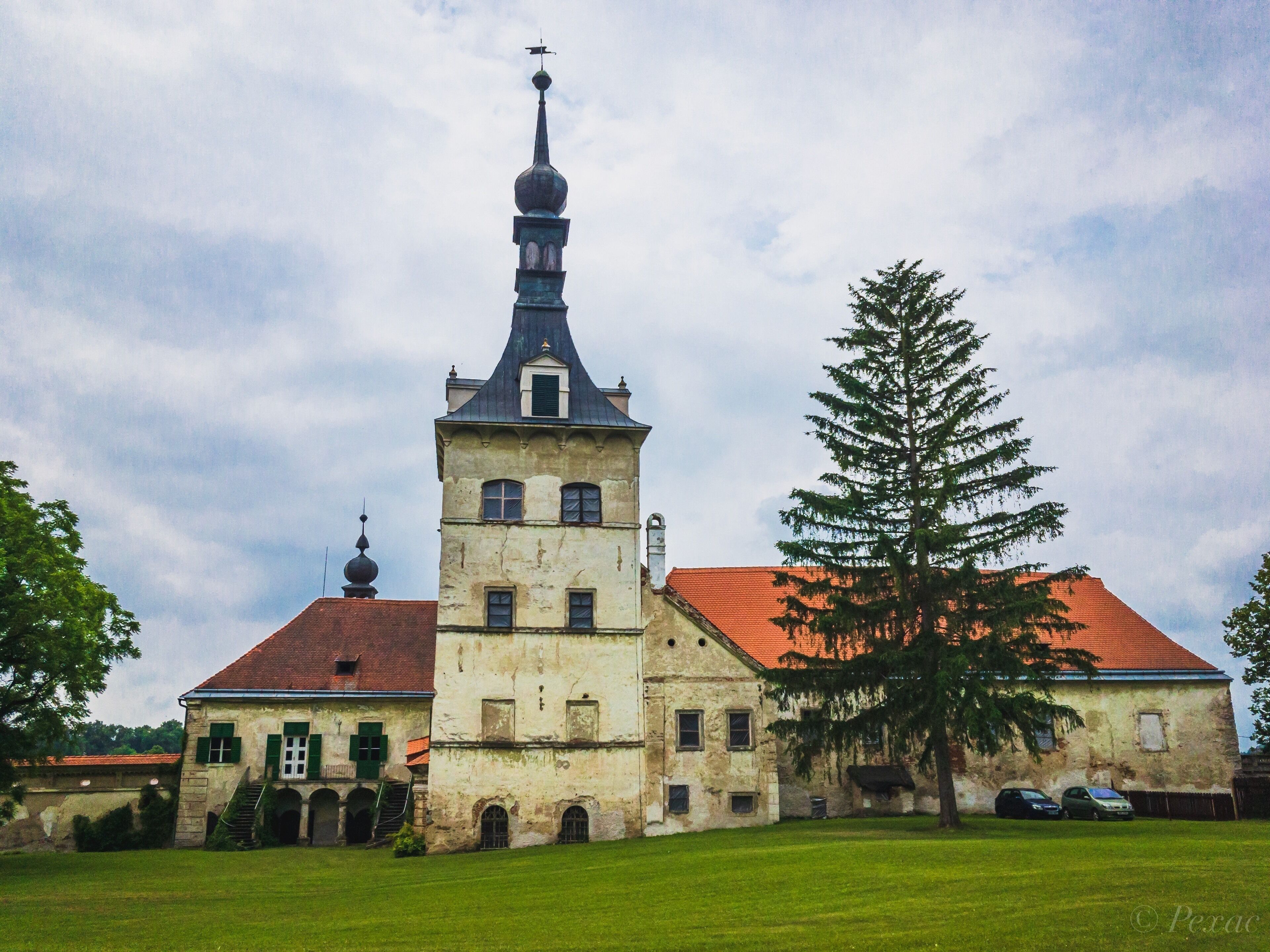 A historic building with a prominent tower and a large tree in front.