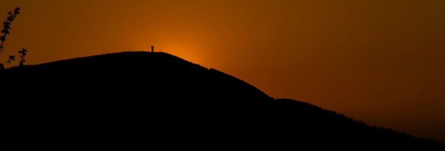 Kukkulan siluetti, jonka huipulla on torni, auringonlaskun taivaalla.