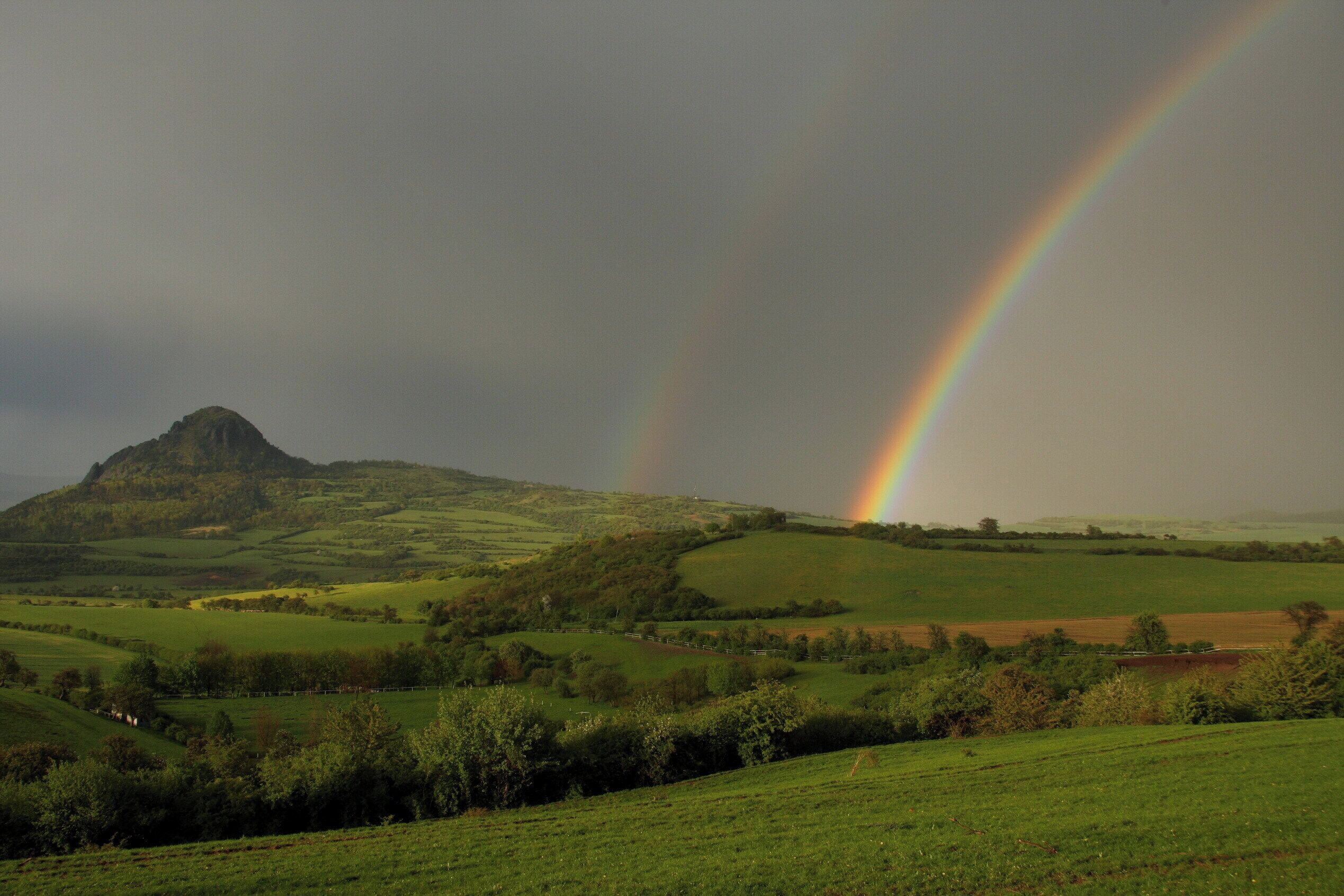 A green landscape with a mountain and a rainbow.