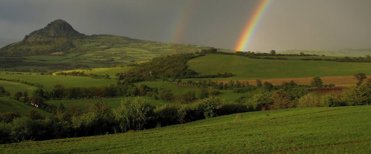 A green landscape with a mountain and a rainbow.