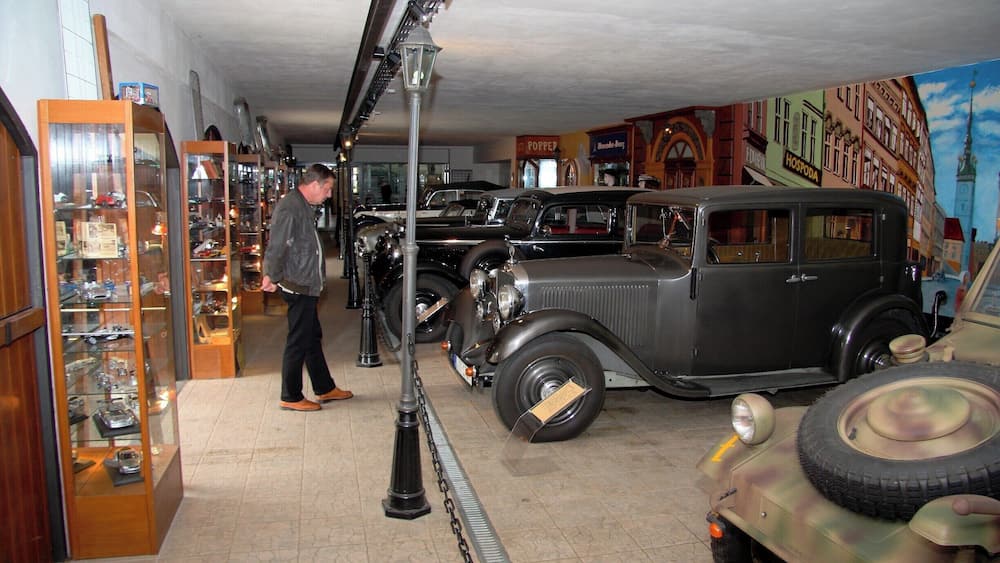 Ein Ausstellungsraum für Oldtimer mit klassischen Autos und einem Wandgemälde einer Stadtansicht.