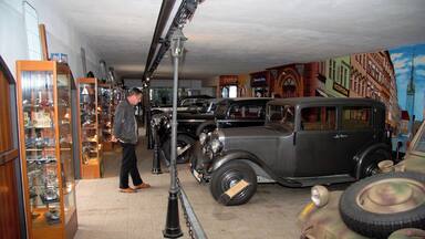 A vintage car showroom with classic cars and a mural of a cityscape.