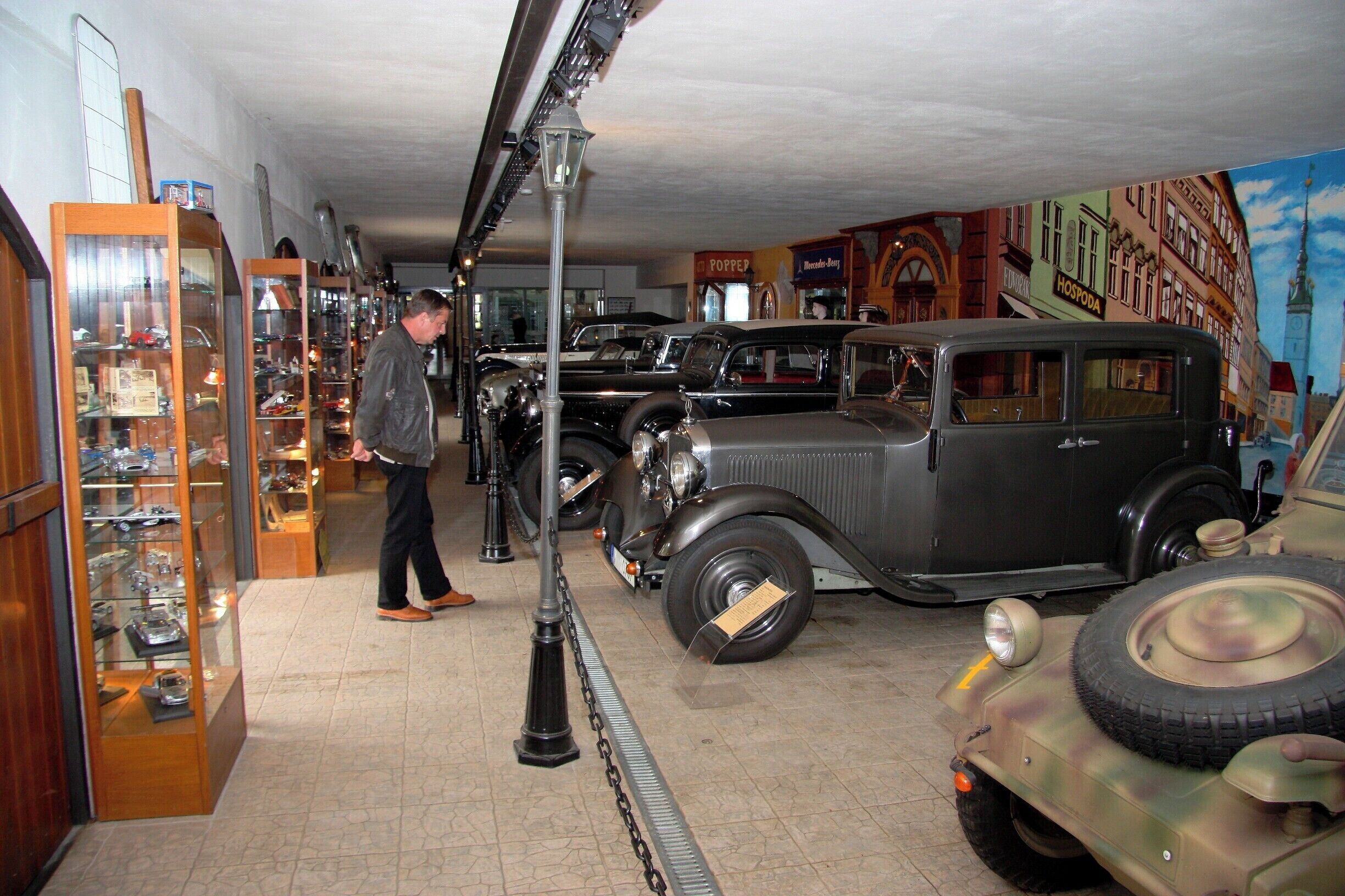 A vintage car showroom with classic cars and a mural of a cityscape.