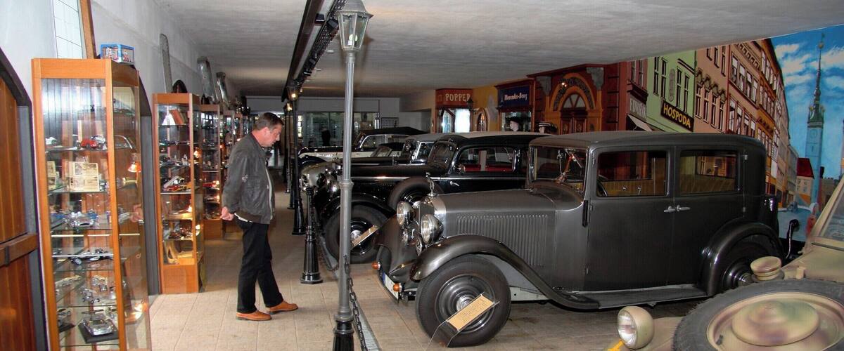 A vintage car showroom with classic cars and a mural of a cityscape.