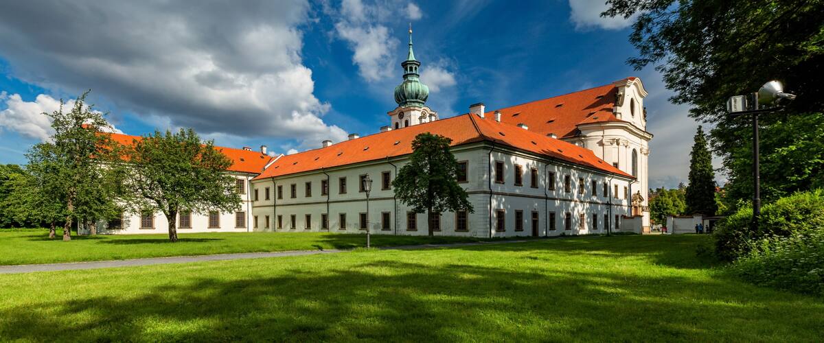 Brevnov, Prague / Czech Republic - June 11 2020: View of the first male monastery in Bohemia standing in a park with green trees on a sunny summer day, blue sky with white clouds.