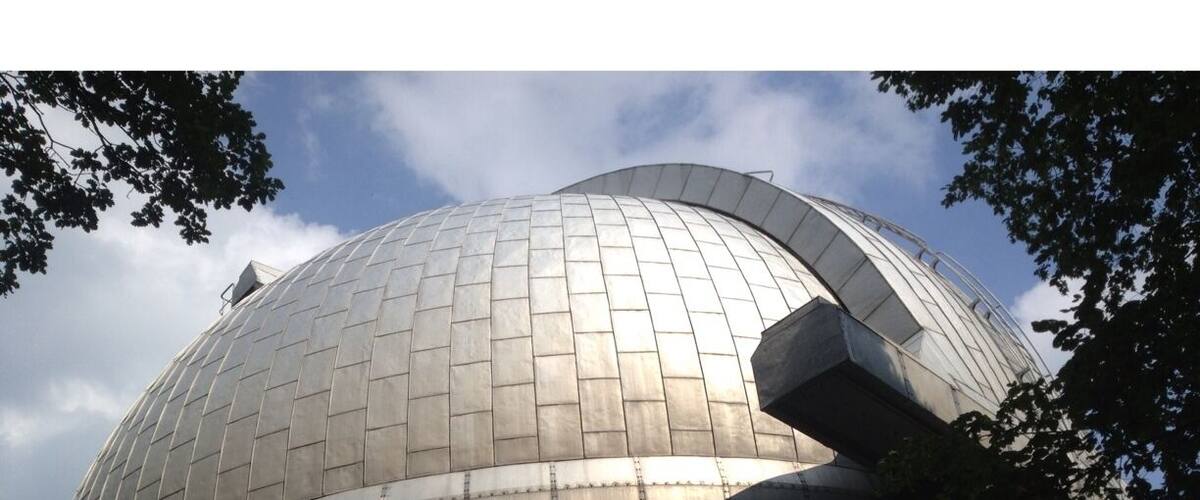 A large metallic dome structure with a grid pattern, surrounded by trees and a clear sky.