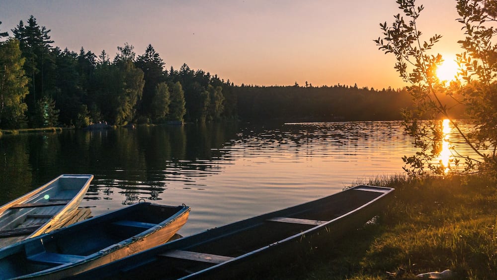 Ein Sonnenuntergang über einem ruhigen See mit Booten, die am Ufer liegen, und einem Wald im Hintergrund.