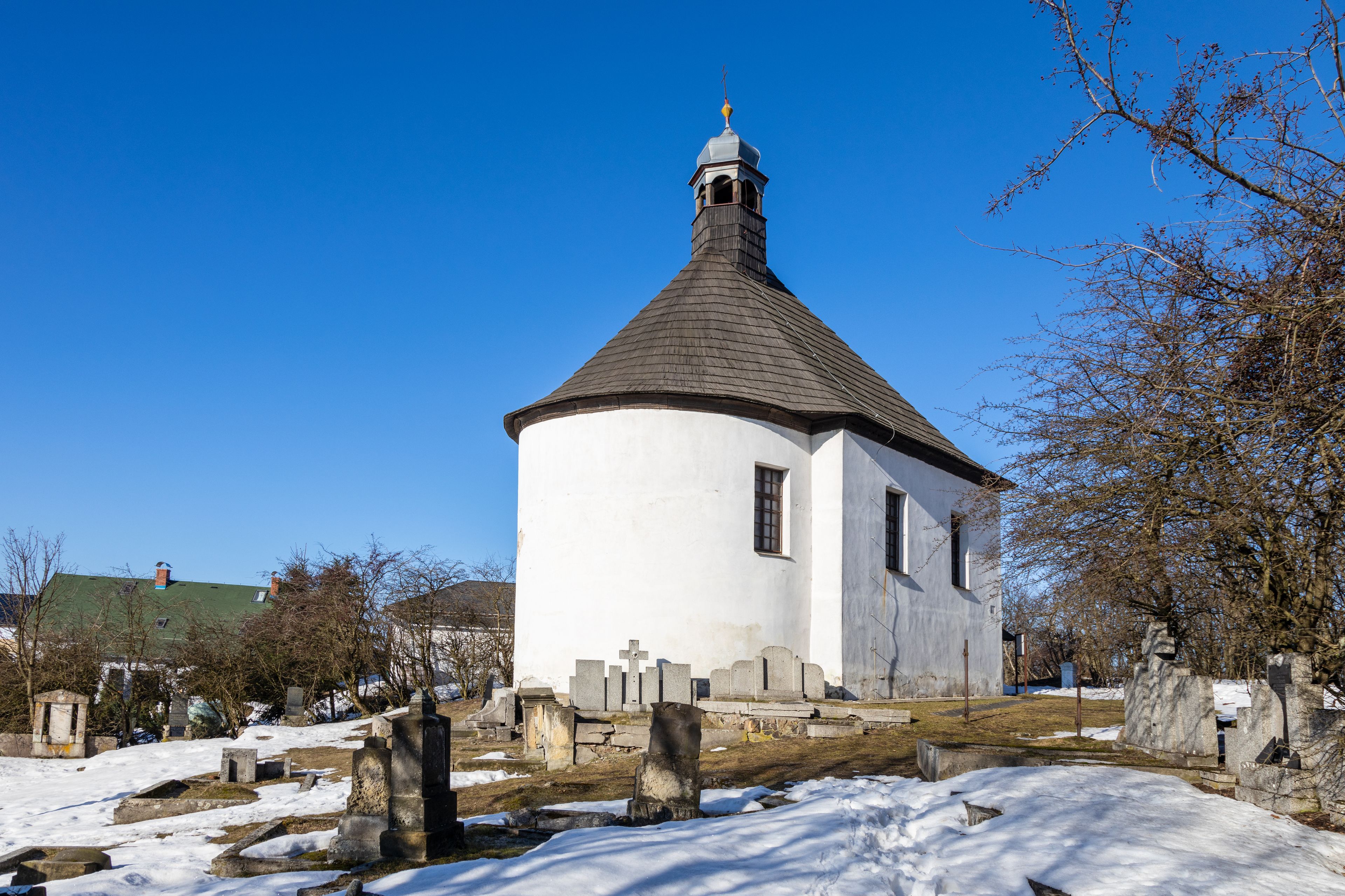A white church with a conical roof and a bell tower, surrounded by snow-covered ground and gravestones.