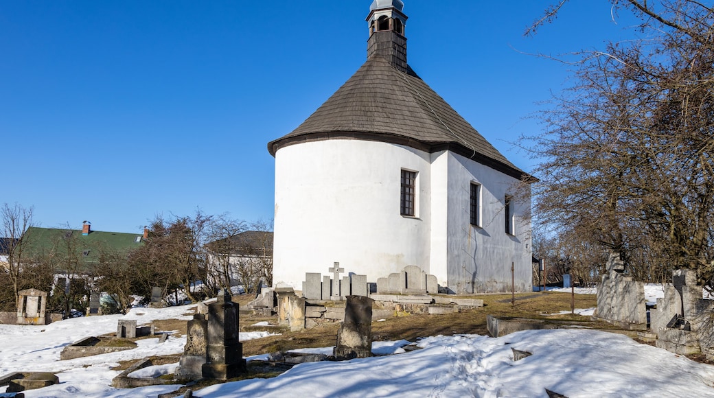 A white church with a conical roof and a bell tower, surrounded by snow-covered ground and gravestones.