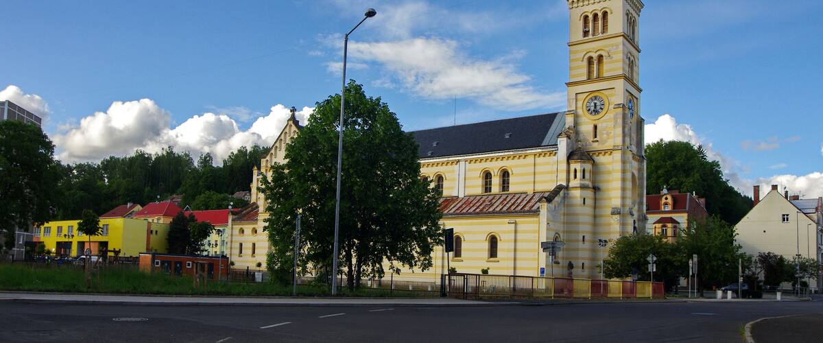 A church with a tall clock tower, surrounded by colorful buildings and trees.