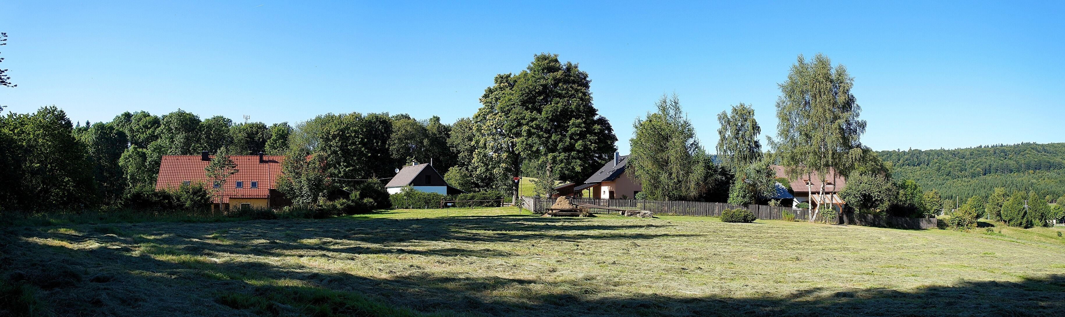 A rural landscape with a red-roofed house, a white house, and a wooden fence.