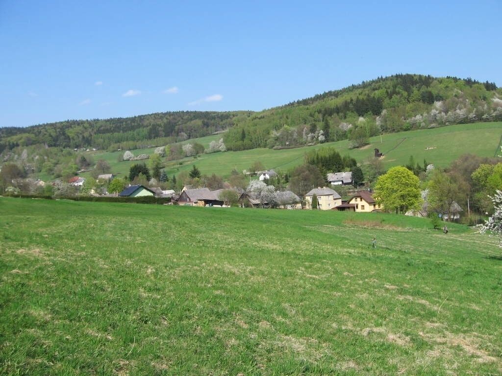 Paisagem rural com colinas ondulantes, algumas casas espalhadas e um amplo campo aberto.