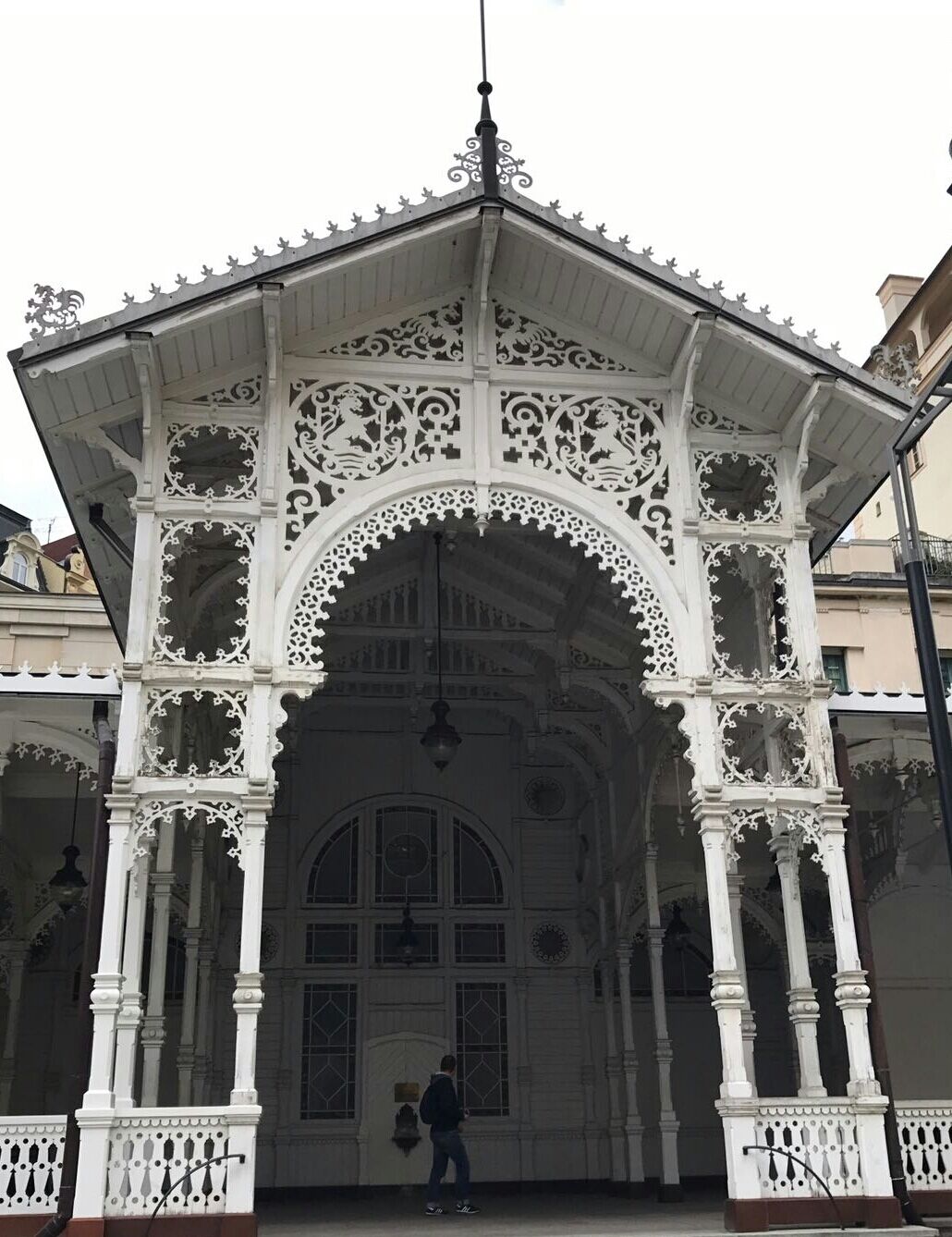 An ornate white gazebo with intricate carvings and a person walking in front.