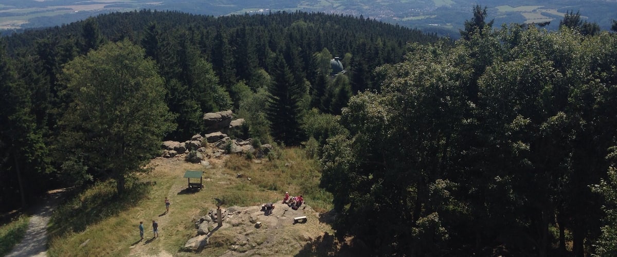 A forested mountain area with a dirt path, rocks, and a small shelter.