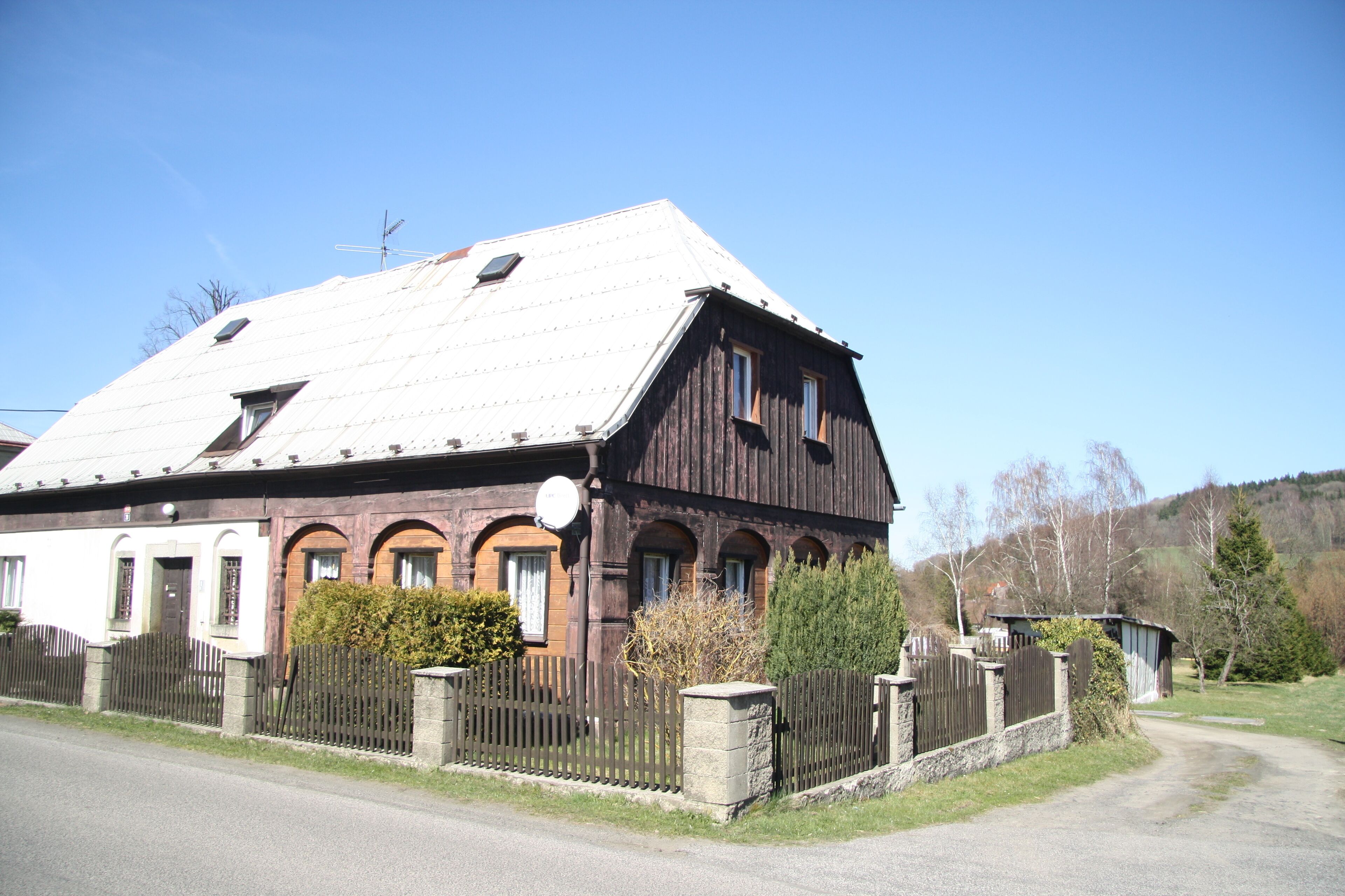 A large wooden barn with a sloped roof, surrounded by a stone fence and a small garden.