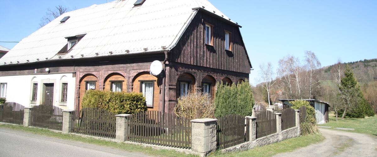 A large wooden barn with a sloped roof, surrounded by a stone fence and a small garden.