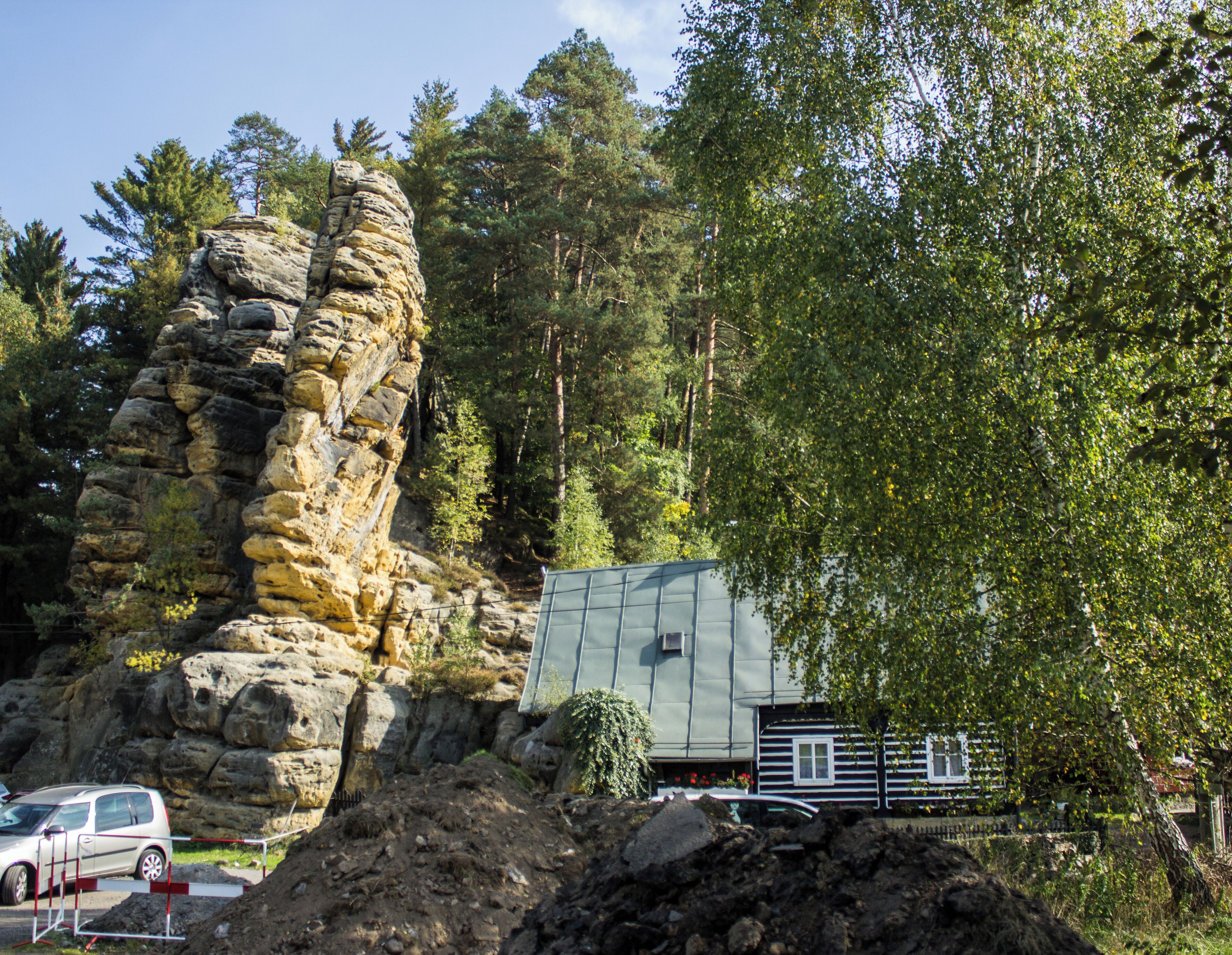 A rocky outcrop, a small cabin, and a car in a forested area.