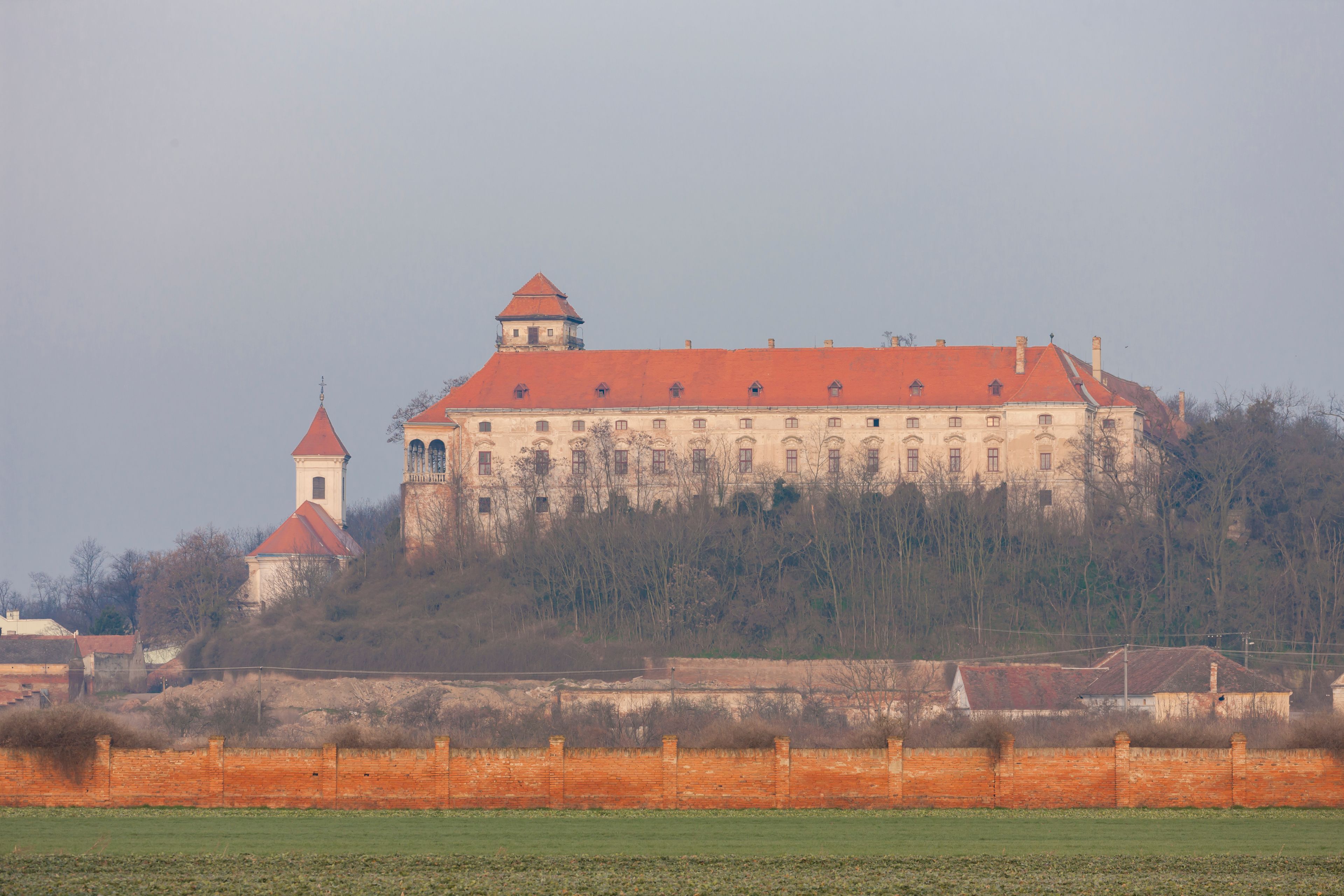 Un castillo grande con techo rojo, una torre más pequeña y una muralla que lo rodea.