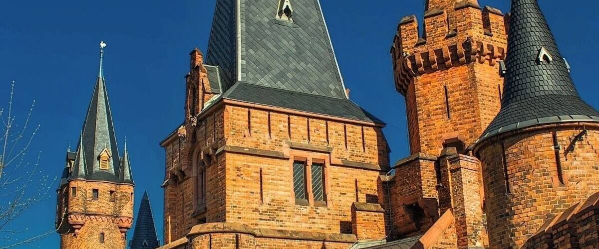 A historic brick building with multiple towers and a steeply pitched roof.