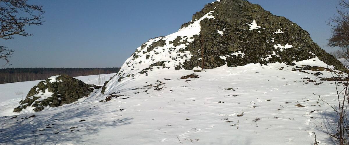 A snow-covered mountain with rocky outcrops and a clear blue sky.