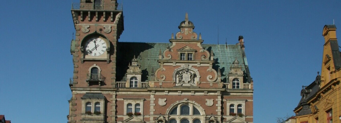 Un edificio histórico con una torre de reloj, ventanas arqueadas y techo verde.