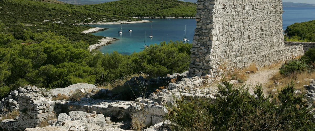 A stone tower by a turquoise bay with sailboats.