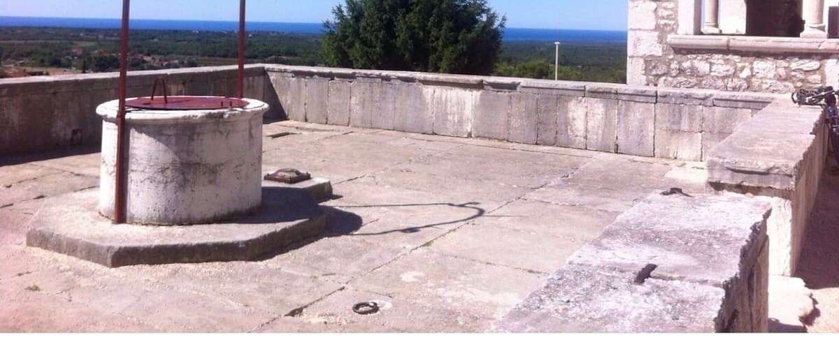 A rooftop with a metal structure, a stone building, and a view of the sea.